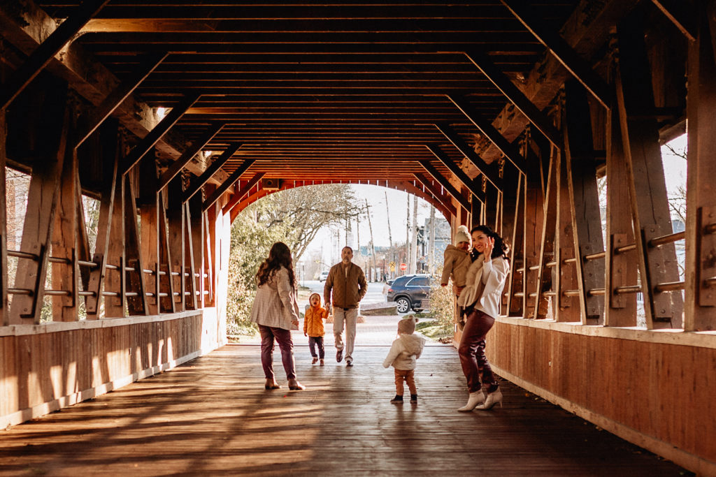 the whole family walks down away from the camera under the covered bridge