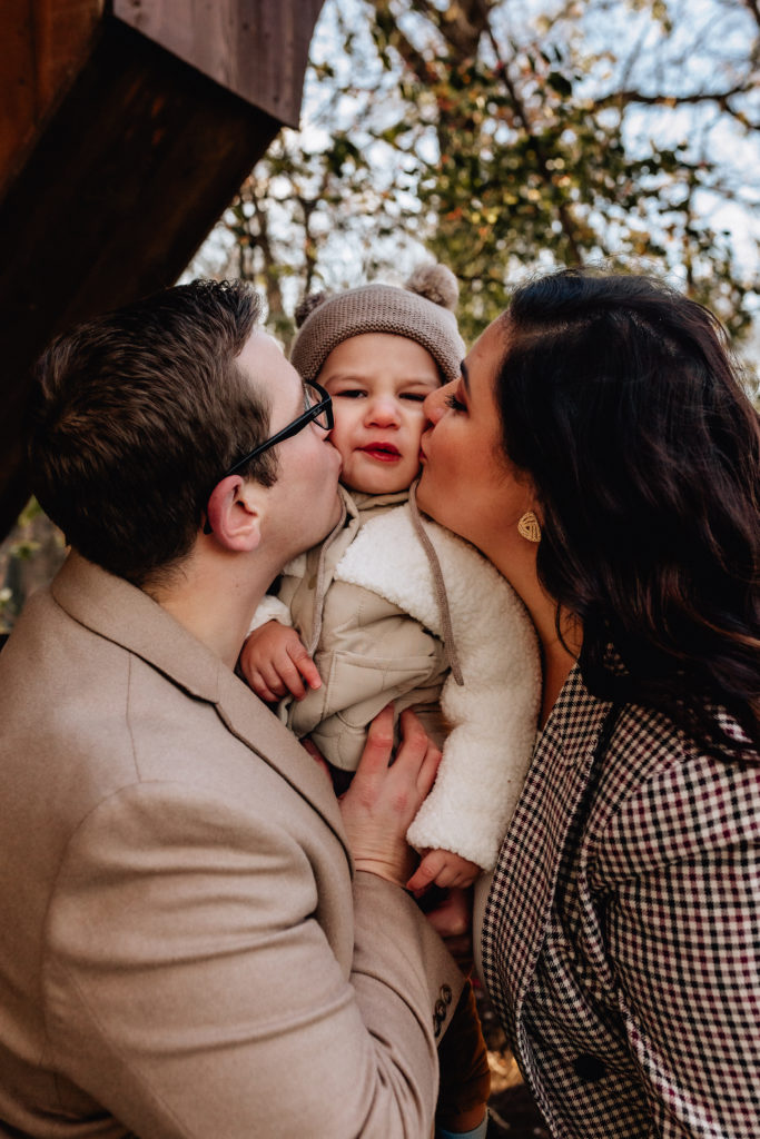 mom and dad squish kiss the cheeks of their toddler on a cold cleveland afternoon