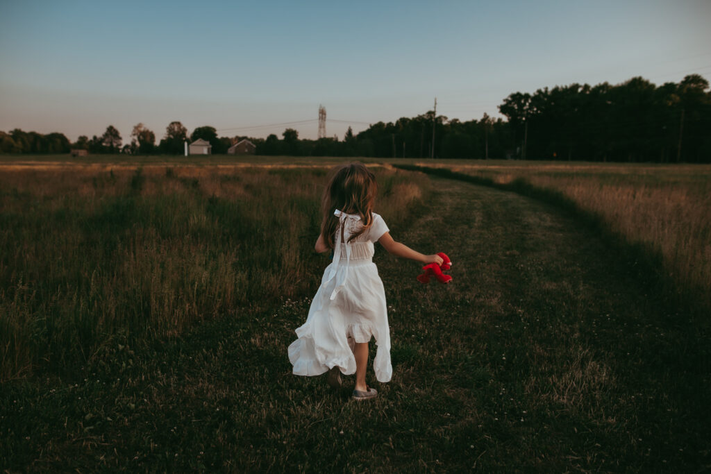 a little girl in a white dress running away from the camera into a field