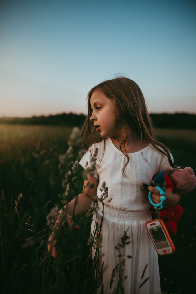 little girl white dress standing in a field of tall grass looking away from camera
