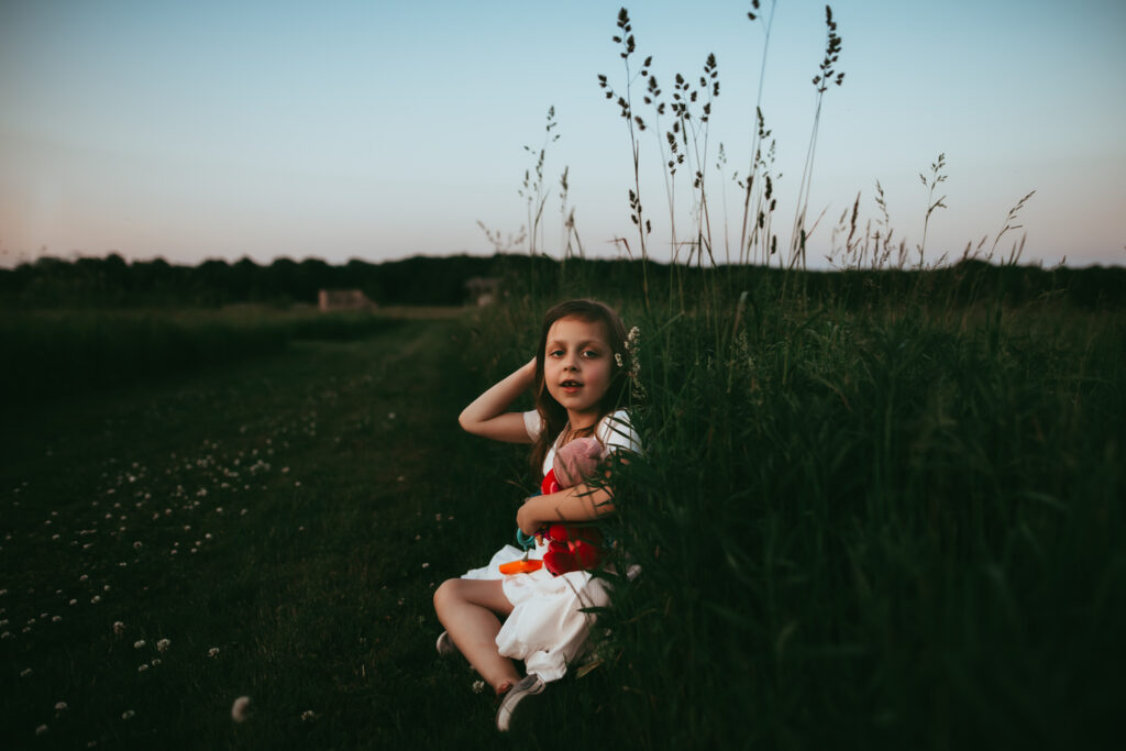 little girl smiling at camera while sitting in a field of tall grass