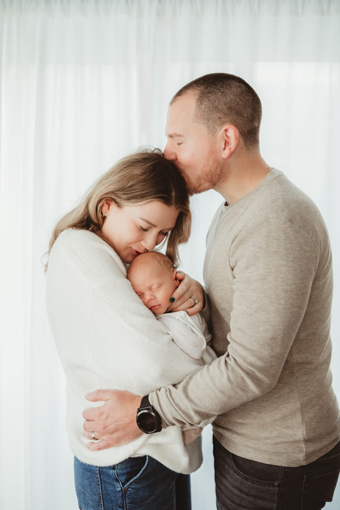 dad kissing mom on the forehead while she snuggles newborn