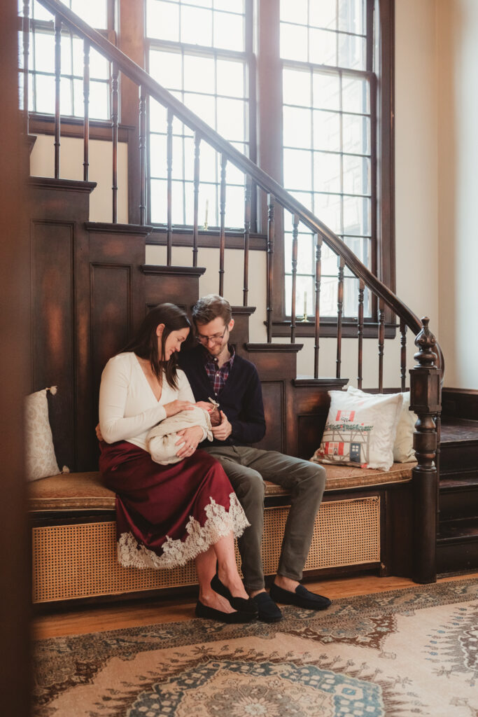 mom and dad snuggle newborn by beautiful staircase