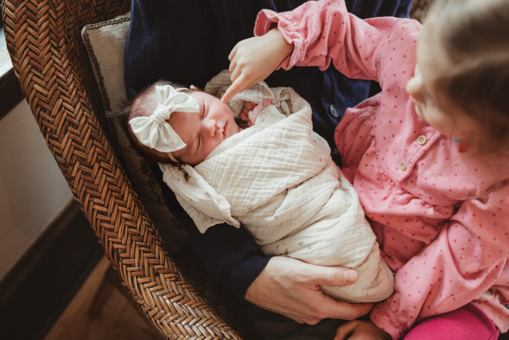 big sister gently touches baby sister's cheek