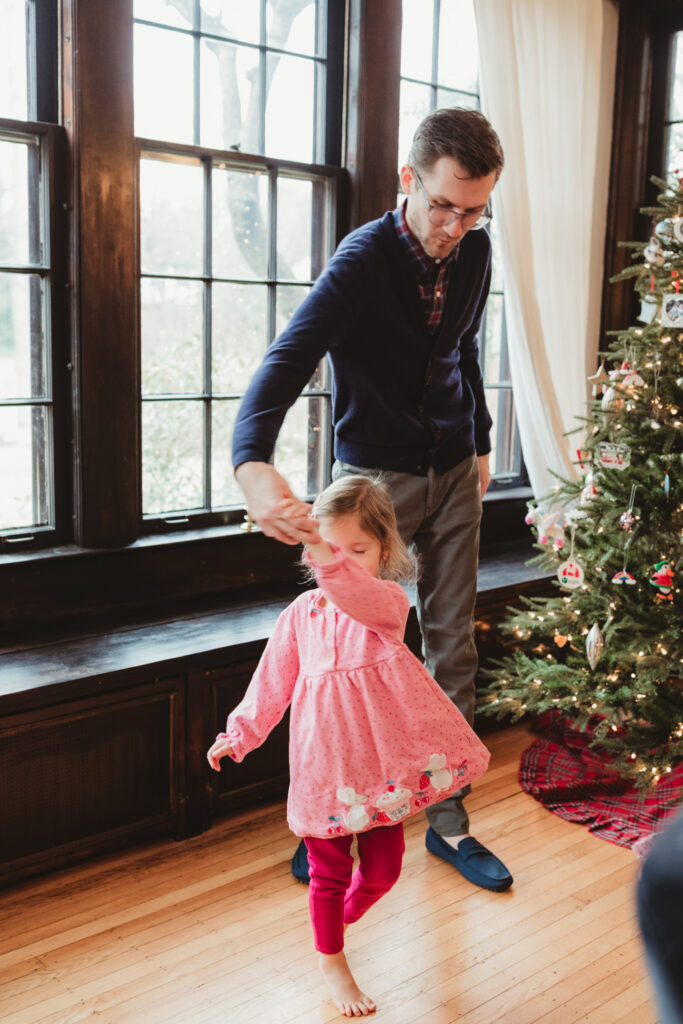 dad twirls big sister by the christmas tree
