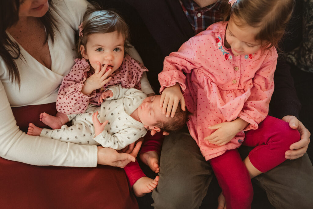 big sisters touch and look at newborn sister