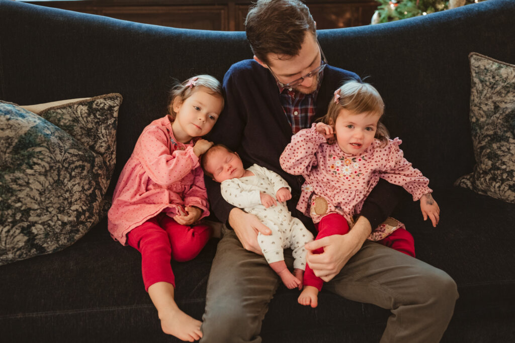 all three little girls snuggle with dad on the couch