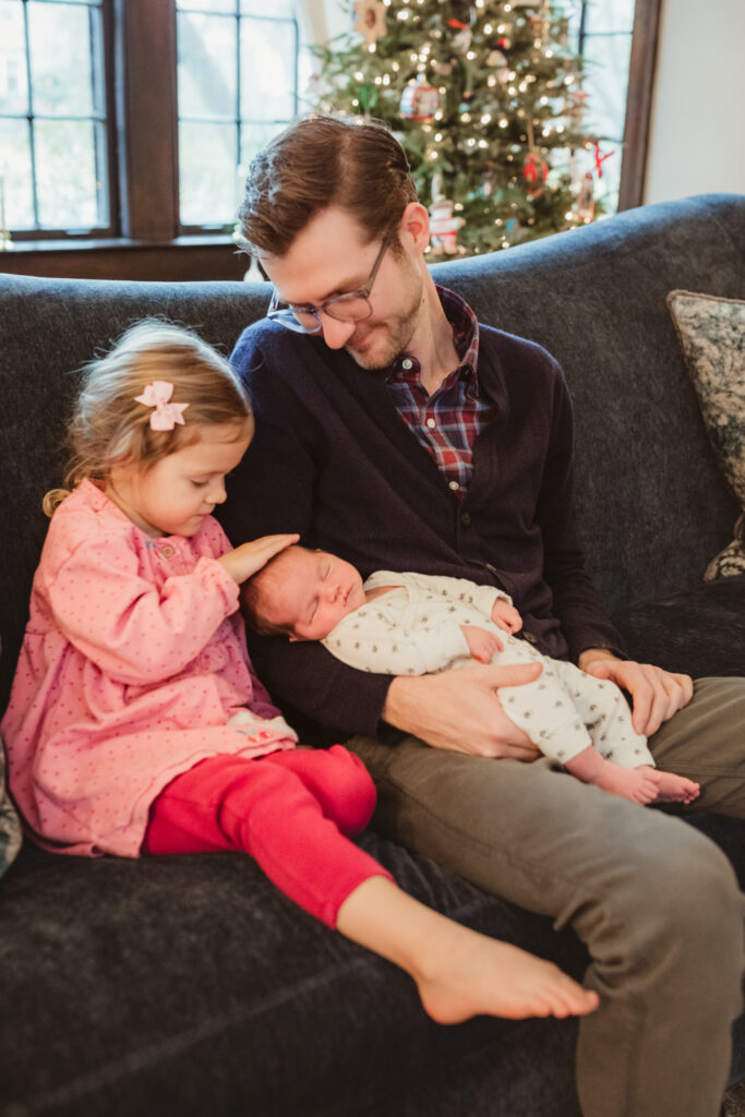 big sister and dad snuggle baby on the couch