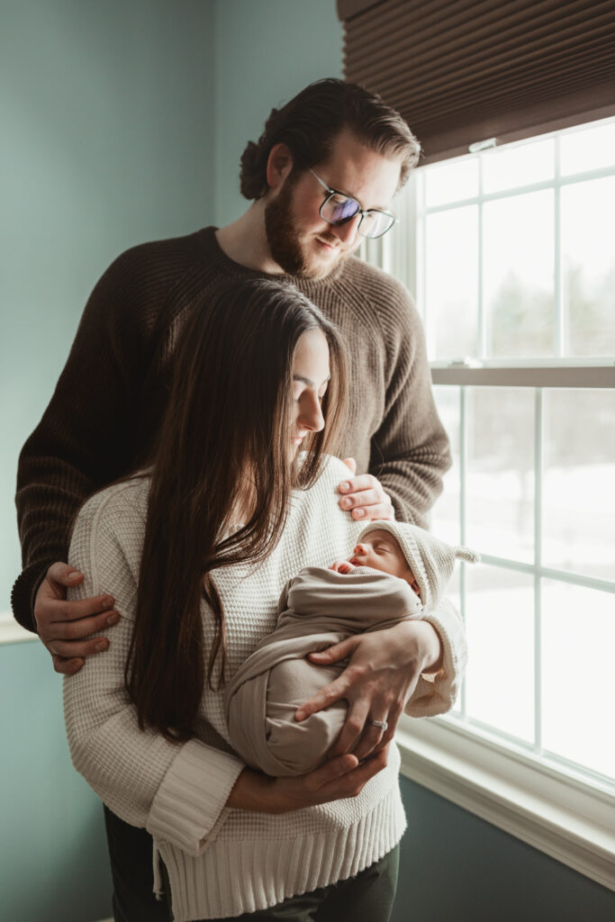 dad holding moms shoulders as she snuggles their baby