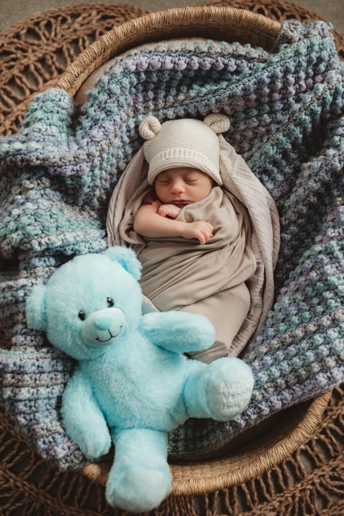 baby snuggled in Moses basket with a blue bear.