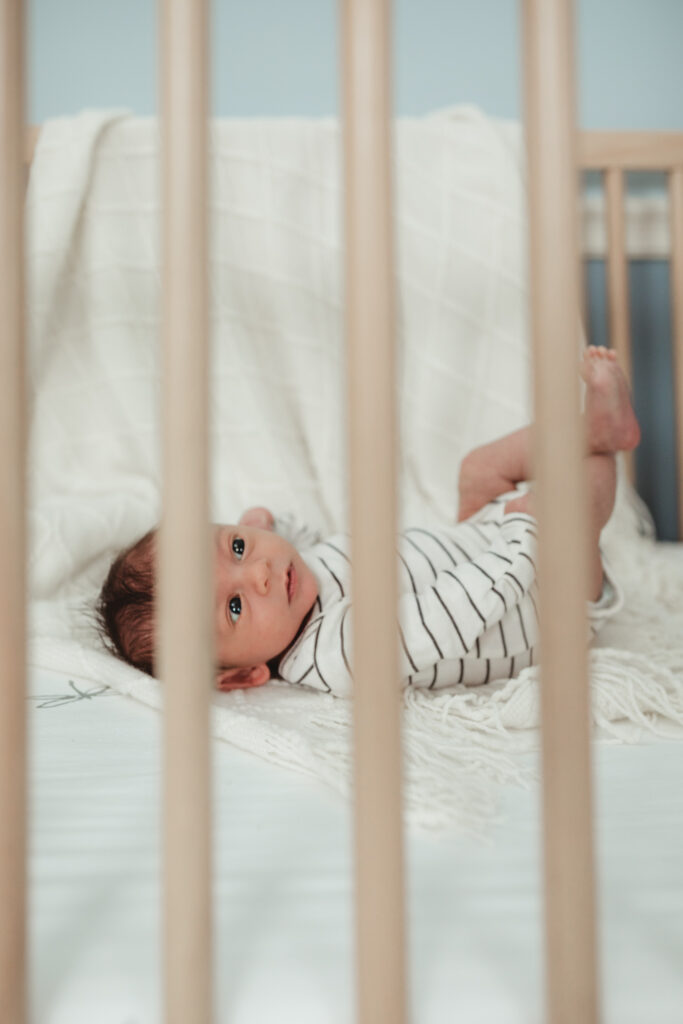 baby in white outfit with black stripes, kicking his feet in the crib