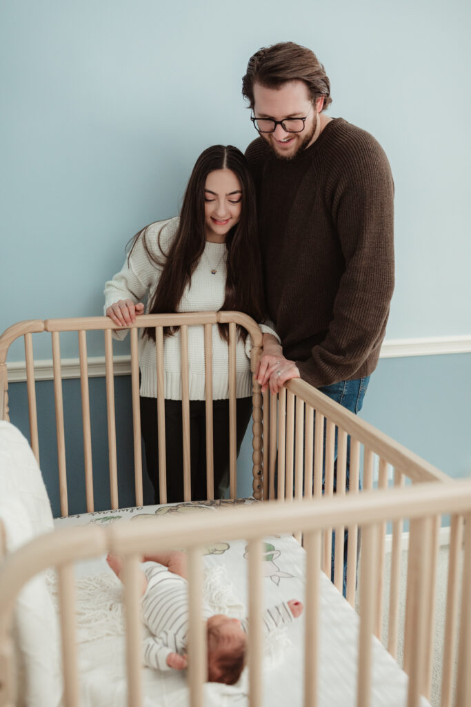 mom and dad looking down at baby while he rests in the crib