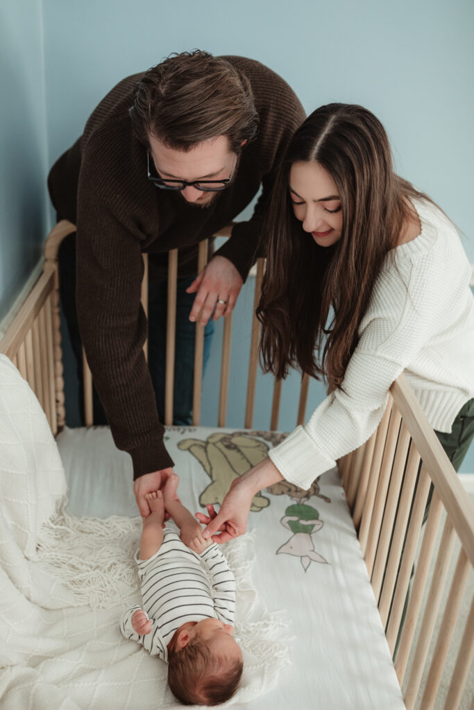mom and dad holding baby's hand and foot while they look at him in his crib