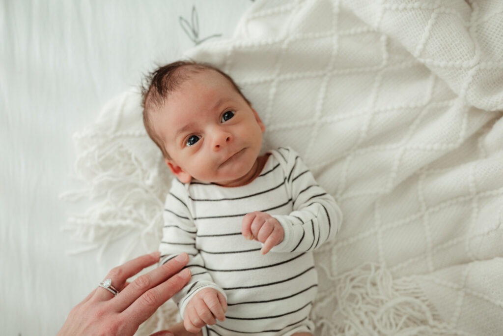 baby looking up past the camera while mom touches him as he lays in his crib