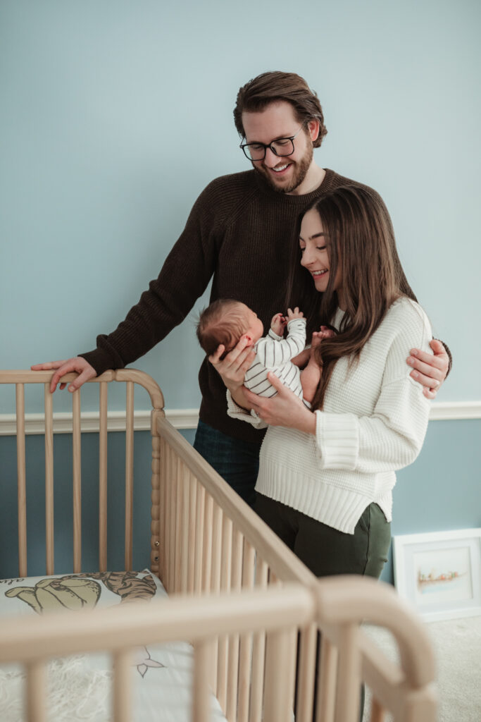 mom holding baby after she picked him up out of the crib, dad looks on.