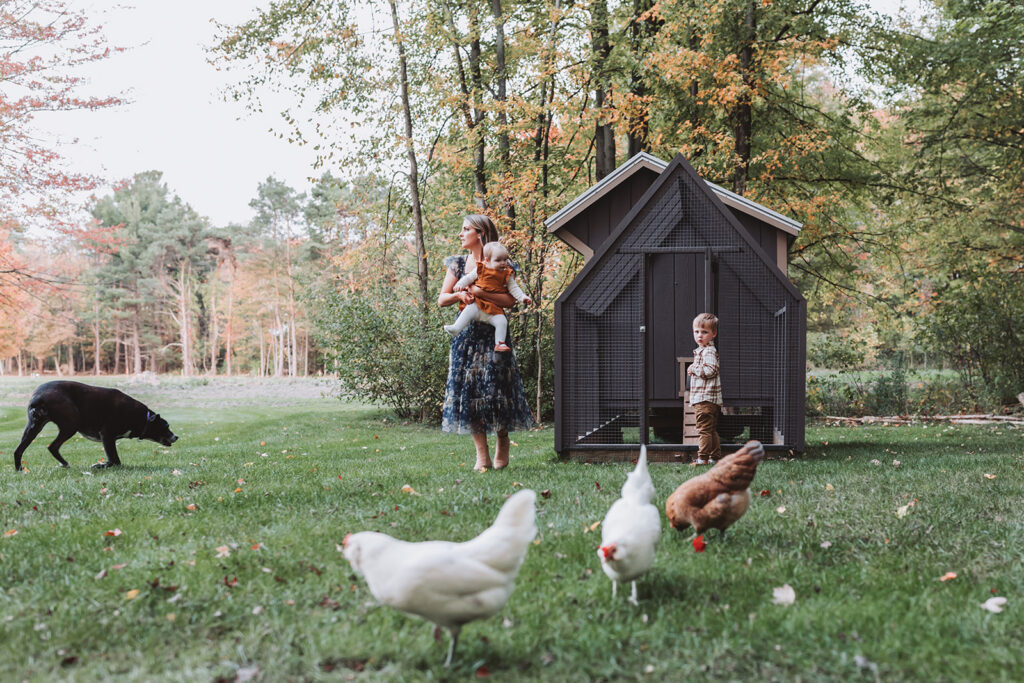 mom looks off camera as she holds her daughter, chickens and her son run amok 