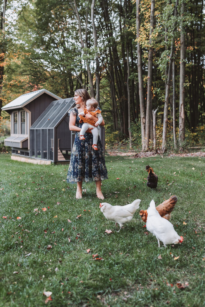 mom looks off camera with chickens around her and daughter in her arms