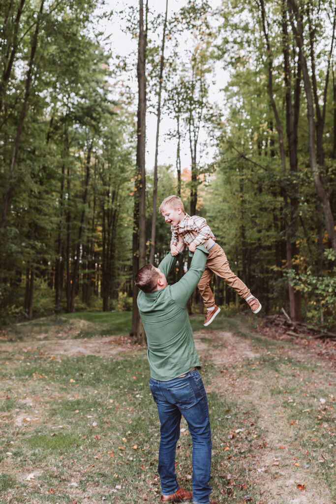 dad lifts little boy high in the air as he laughs