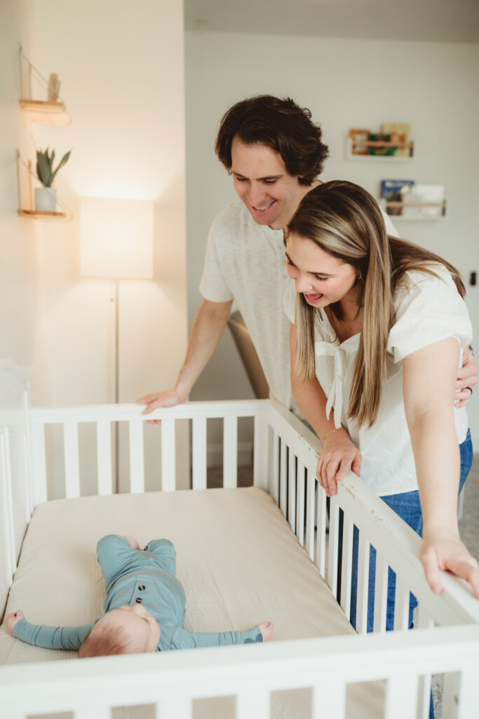 mom and dad look down with smiles at their baby in this crib