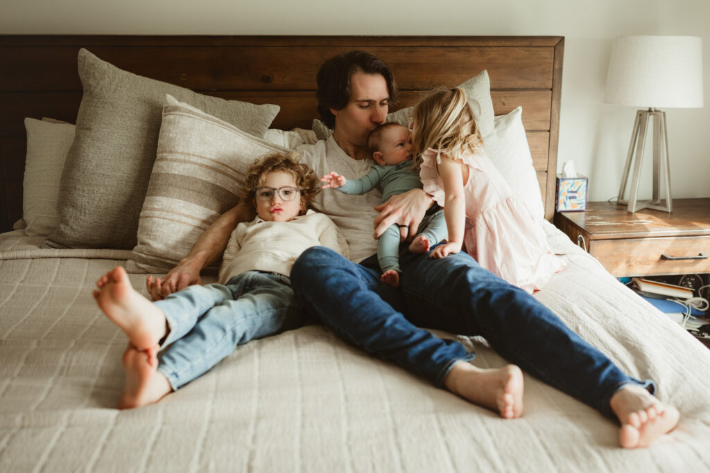 dad snuggles on the bed with all his kids