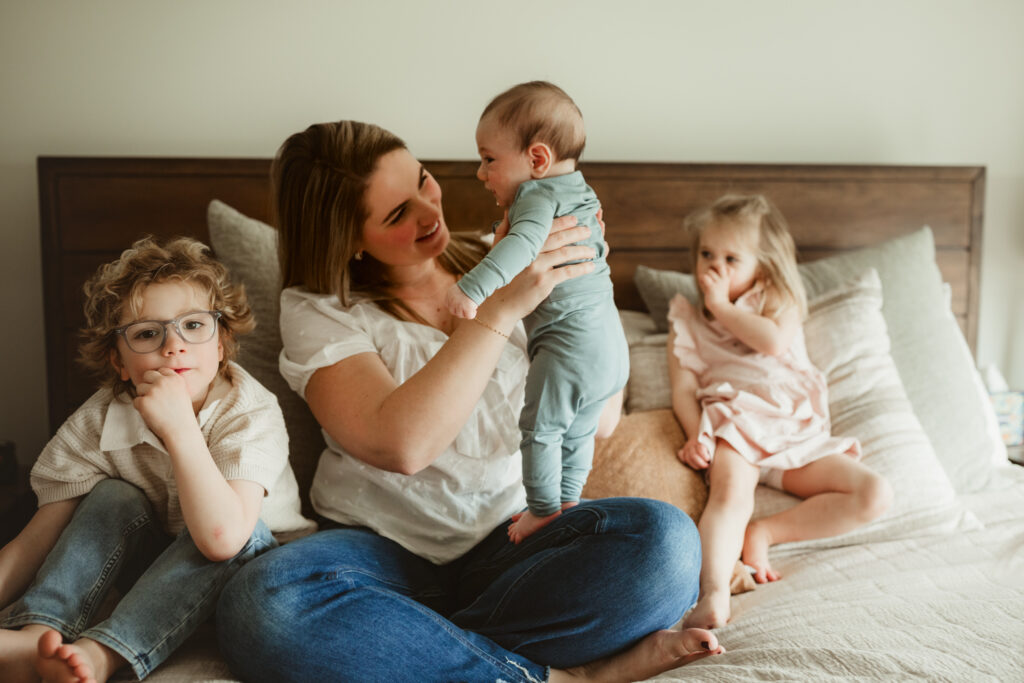 mom snuggles baby and older children on the bed