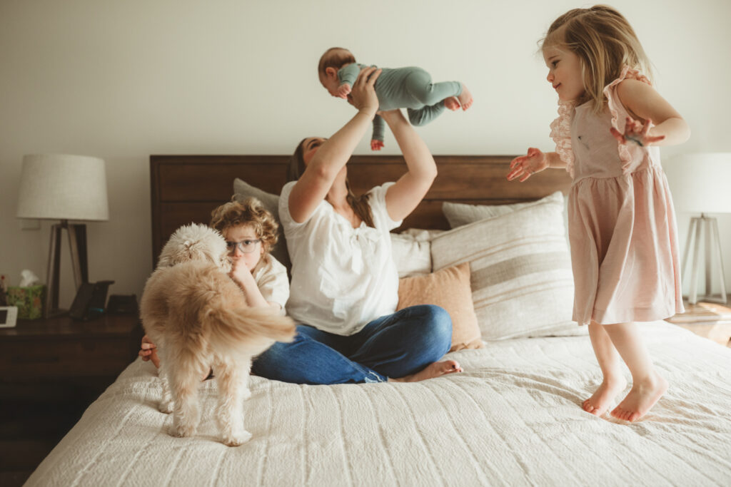 mom airplanes baby while the kids bounce on the bed, including family dog