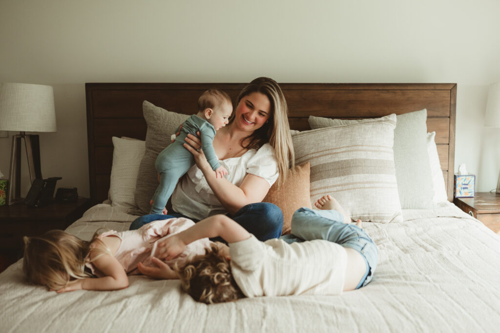 mom smiles at kids antics after bouncing on the bed